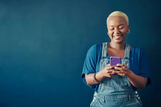 Photo of Smiling woman in overalls texting on her phone against a blue background