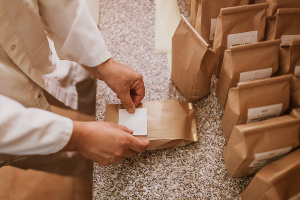 Man applying label on paper bags in mill Man sticking blank label on freshly filled flour brown paper packages on table labeling stock pictures, royalty-free photos & images