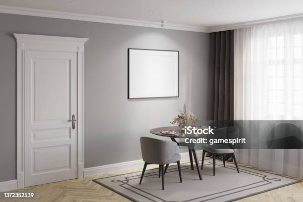 A Gray Modern Classic Dining Room With A Blank Illuminated Horizontal Poster Above A Round Wooden Table With Two Elegant Chairs A White Classic Door Dark Gray Curtains Near The Window Stock Photo - Download Image Now