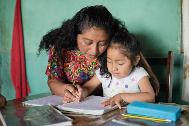 испаноязычная мама помогает своей маленькой дочери делать домашнее задание - мама учит дочь читать и писать дома - семья майя дома - guatemalan culture central america mother traditional culture стоковые фото и изображения