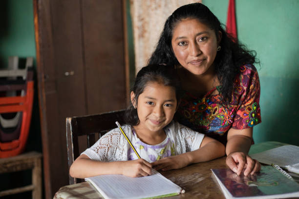 hispanische mutter, die ihrer kleinen tochter hilft, ihre hausaufgaben zu machen - mama bringt ihrer tochter zu hause das lesen und schreiben bei - maya-familie zu hause - peruanische kultur stock-fotos und bilder