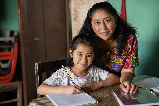 Mamá hispana ayudando a su pequeña hija a hacer su tarea - Mamá enseñando a su hija a leer y escribir en casa - Familia maya en casa photo