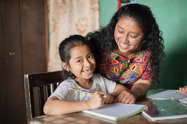 испаноязычная мама помогает своей маленькой дочери делать домашнее задание - мама учит дочь читать и писать дома - семья майя дома - guatemalan culture central america mother traditional culture стоковые фото и изображения