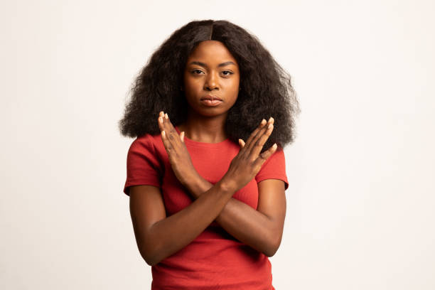Portrait Of Young Black Female Showing Stop Gesture With Crossed Hands Portrait Of Young Black Female Showing Stop Gesture With Crossed Hands, Serious Millennial African American Woman Refusing Something While Posing Over White Studio Background, Copy Space bushy stock pictures, royalty-free photos & images