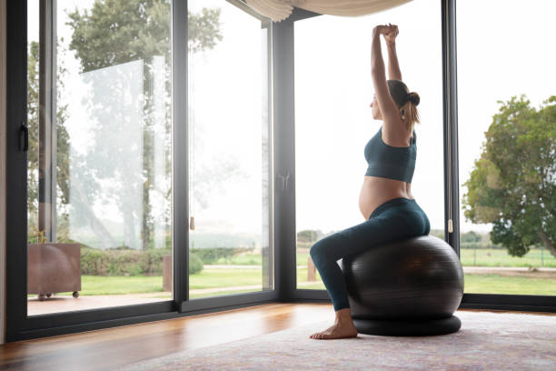 femme enceinte blonde pratiquant le yoga dans le salon à côté des fenêtres - yoga ball photos et images de collection