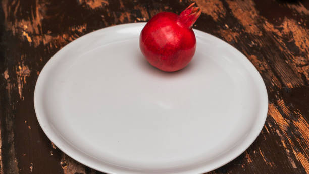 istock Whole red pomegranate on big white plate. Fresh raw organic garnet fruit. Pomegranate is a symbol of Judaism. 1372359615