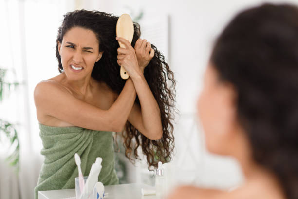 istock Frustrated young lady having problem brushing her tangled hair in front of mirror at home, copy space 1372360397