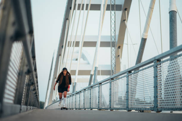 istock Young woman riding her longboard on the bridge 1372360496