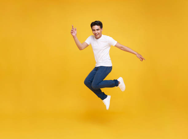 Happy Asian man smiling and jumping while celebrating success isolated over yellow background. stock photo