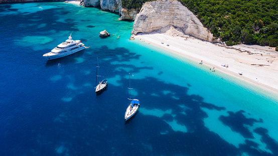 Amazing coast with beautiful beach and forest around on Ionian sea and anchored yacht and sailboats in bay. Kefalonia island, Fteri beach, Greece