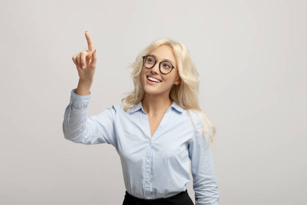 Happy female entrepreneur pushing button on virtual screen over light grey studio background, mockup for design Happy female entrepreneur pushing button on virtual screen over light grey studio background, mockup for design. Young businesswoman interacting with touchscreen clicking screen stock pictures, royalty-free photos & images