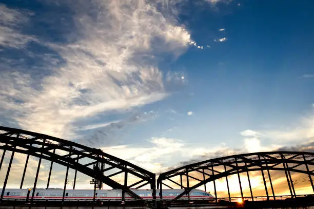 An express train travels at the bottom of the image over an arched bridge with sky in the background