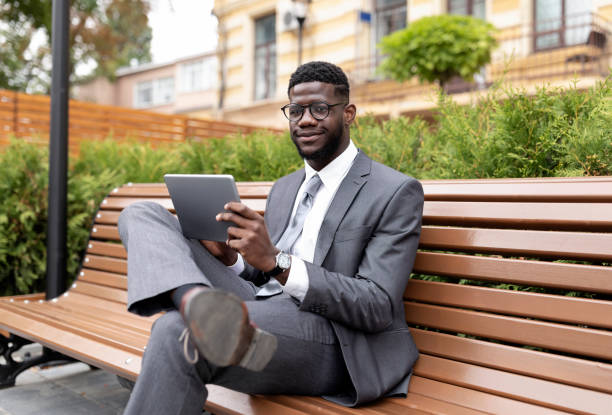 istock Confident african american entrepreneur using digital tablet, browsing news while sitting on the bench outdoors 1372362894