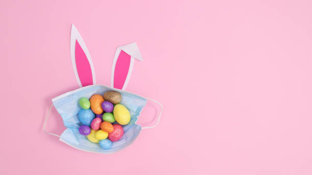 istock Face mask with colorful Easter eggs and bunny ears on pastel pink background. Creative copy space flat lay 1372365323