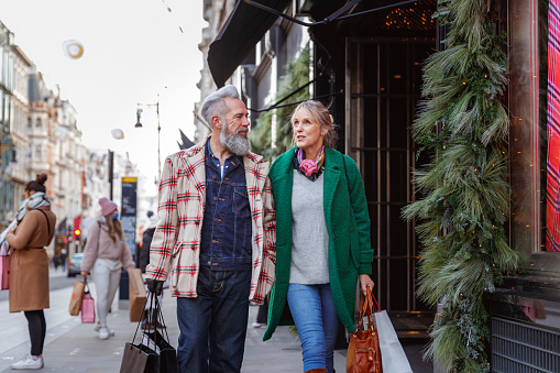 A vibrant senior couple walk and talk happily along a city street while shopping for Christmas gifts in the city.