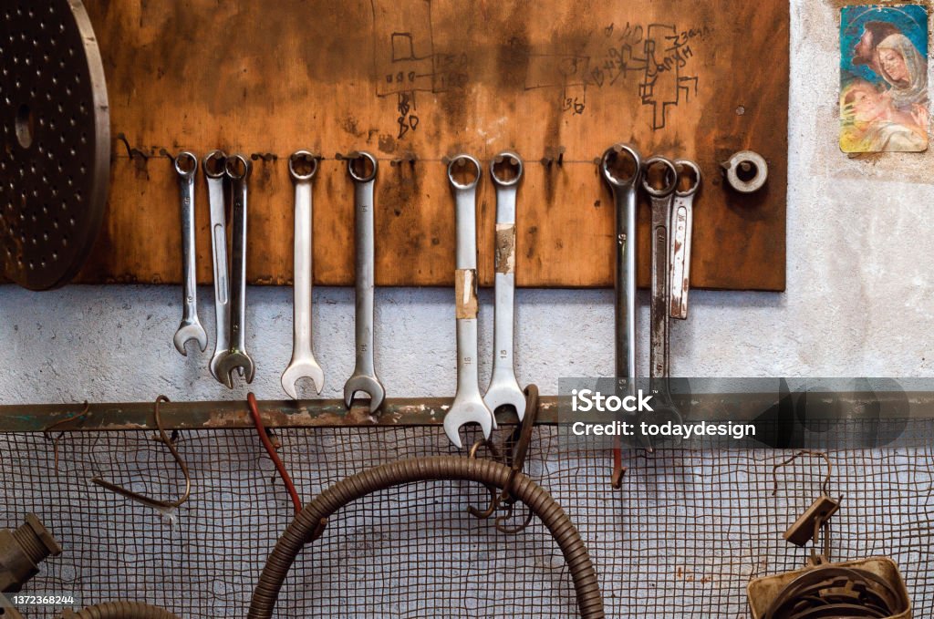Old wrenches hang on the wall in the old workshop. The atmosphere of the old garage. Old wrenches hang on wall in  old workshop. The atmosphere of  old garage. Adjusting Stock Photo