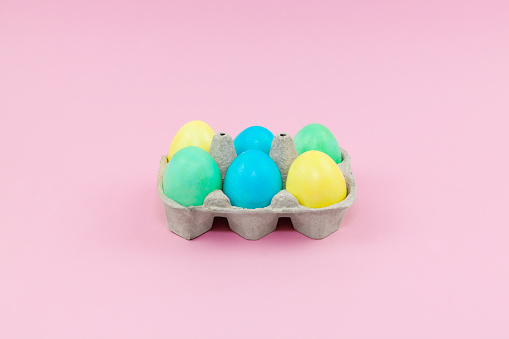 Box with colorful Easter eggs on a pink background
