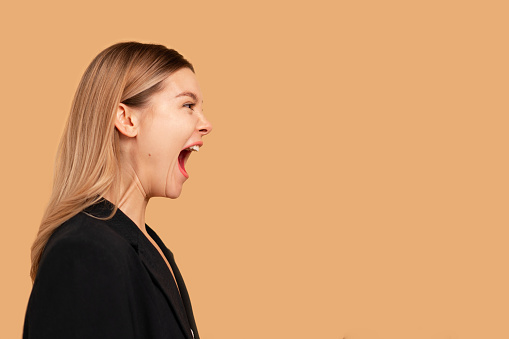 Young business woman screaming loud side view isolated on color background. Caucasian female business person aggressive yelling. Business woman shouting side dressed black formal wear jacket