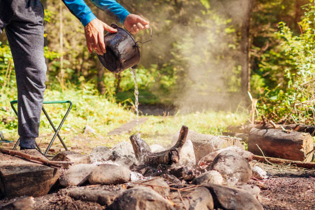 istock Man extinguishing campfire with water from cauldron in summer forest. Put out campfire. Traveling fire safety rules 1372368382