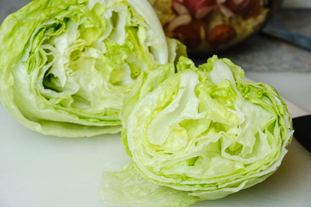 cut bulb of fresh iceberg lettuce also known as crisphead lettuce on a cutting board - iceberg lettuce imagens e fotografias de stock