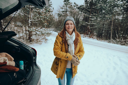 Smiling and happy young woman having a road trip on a beautiful snowy winter day in nature