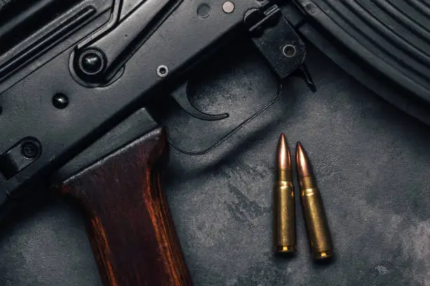 Two bullets and Kalashnikov assault rifle on gray concrete background, top view. Cartridge 7.62 caliber for ak 47 closeup