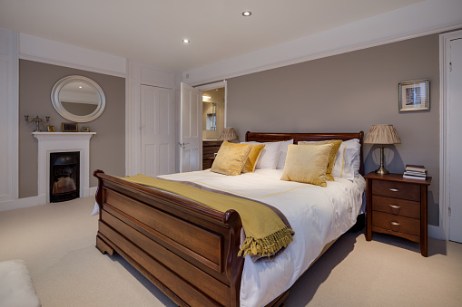 Traditional looking modern bedroom within renovated luxury home with wooden bed, side ables, open fire and brightly illuminated.