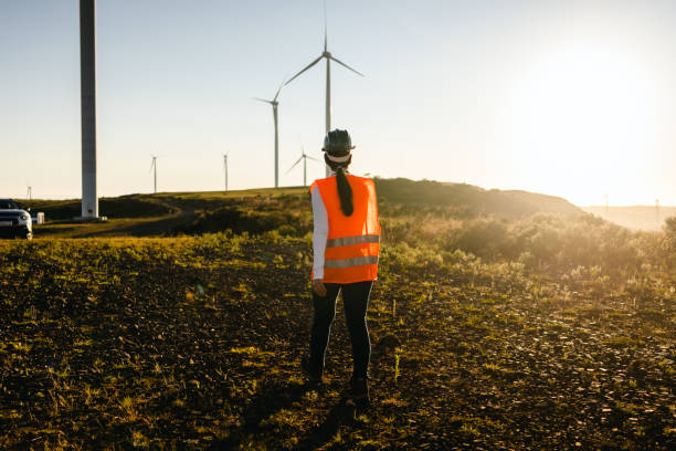 Female worker walking towards car in wind power field Female worker walking towards car in wind power field industrial windmill stock pictures, royalty-free photos & images