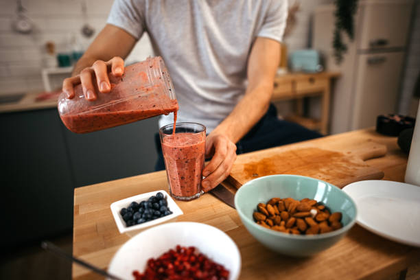 istock Man pouring smoothie in glass while sitting in kitchen 1372373605