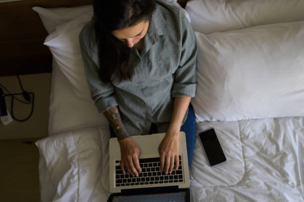 istock Sitting on her white sheets, the girl attentively types 1372374116
