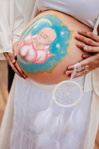 Pregnant woman with painted with question mark and gender symbols paint on bare tummy.