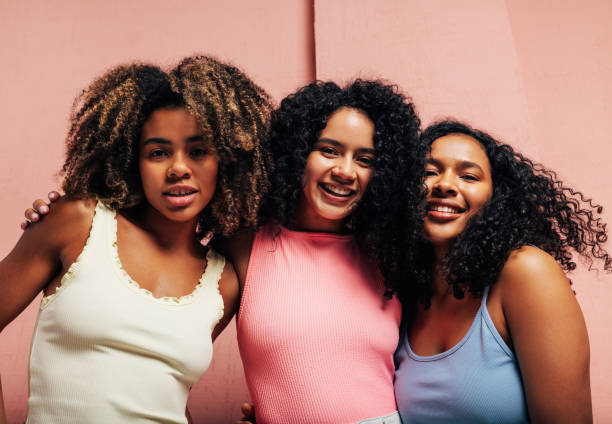 istock Three girlfriends in bright casual hugging each other looking at camera against a pink wall 1372376247