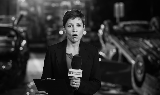 Portrait of female reporter covering news of car accident on road at night. Reporting and news concept.