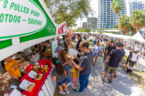 Miami, Florida, USA - February 21, 2022: Nationals and Internationals tourists enjoying President's Day National Holidays at Coconut Art Festival; walking, eating and drinking different types of fast food offering in food trucks in a sunny summer day in Coconut Grove park.