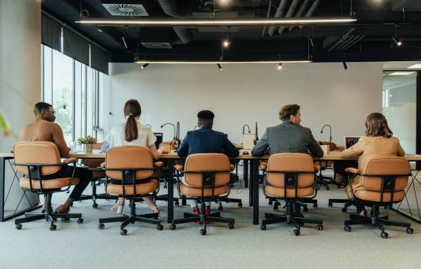 vue arrière d’un groupe méconnaissable de gens d’affaires assis en rangée et travaillant sur des ordinateurs dans un bureau à aire ouverte - five in a row photos et images de collection