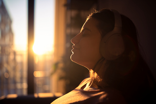 Close-up of woman with headphones enjoying music on sunrise.