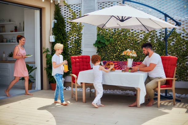 bambini felici che aiutano la madre a preparare la tavola nel patio estivo, stile di vita familiare - party umbrella foto e immagini stock