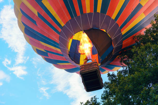 colorido globo aerostático con personas en una cesta se eleva al cielo entre los árboles - globo aerostático fotografías e imágenes de stock