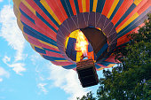 Colorful hot air balloon with people in a basket rises to the sky among the trees