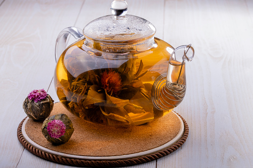 Green oolong tea tied into a flower brewed in a glass teapot close-up