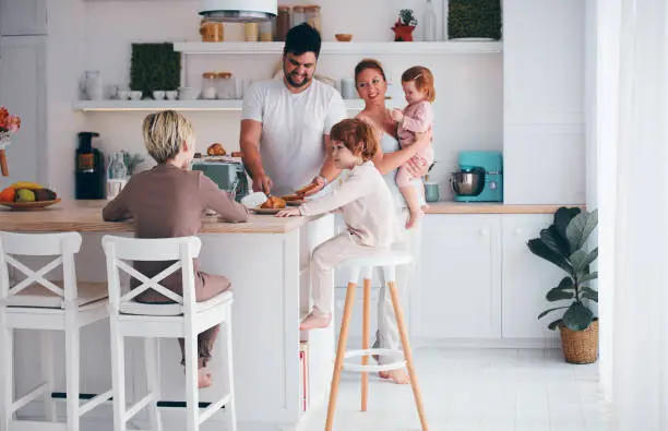 Photo of happy family with three kids having breakfast in the kitchen in the morning