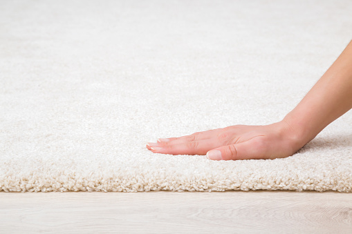 Young adult woman hand touching new white fluffy carpet surface on laminate floor. Closeup. Checking softness. Side view.