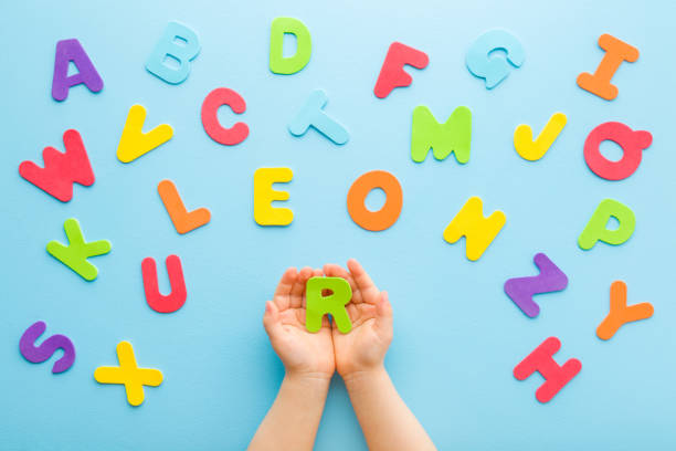 Toddler boy hands holding R letter. Colorful letters on light blue table background. Pastel color. Time to learning English alphabet. Point of view shot. Closeup. Top down view. stock photo