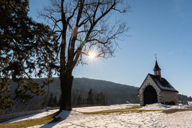 Sun rays behind a little chapel in Gais in Switzerland Gais, Appenzell, Switzerland, January 26, 2022 Bright shining sun and a tiny chapel on a snow covered hill appenzell stock pictures, royalty-free photos & images