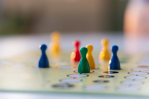 close up view of a board game with colorful game pieces -  focus on one game piece with reduced field of depth. Blurred foreground and blurred background. Evening sunlight is reflecting on the board
