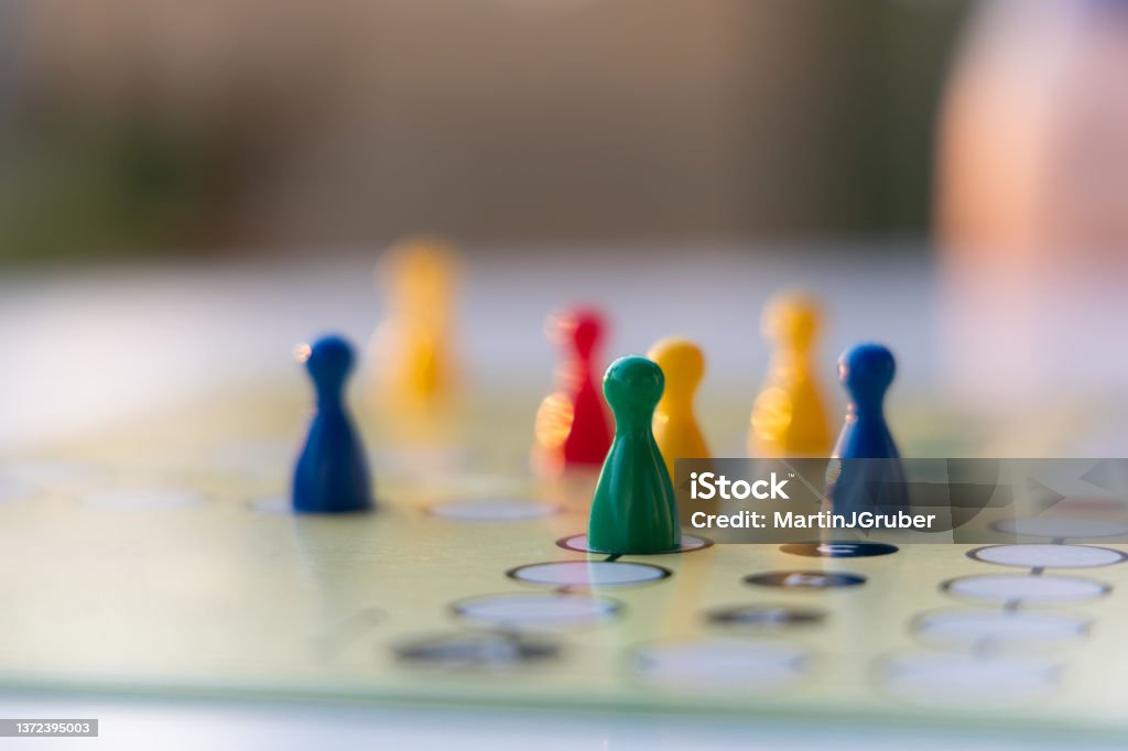 board game close up view of a board game with colorful game pieces -  focus on one game piece with reduced field of depth. Blurred foreground and blurred background. Evening sunlight is reflecting on the board Board Game Stock Photo