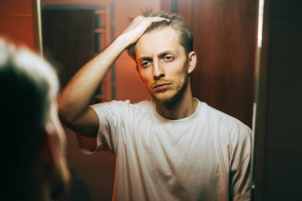 istock Young caucasian man standing in front mirror touching face and looking on himself. 1372400679