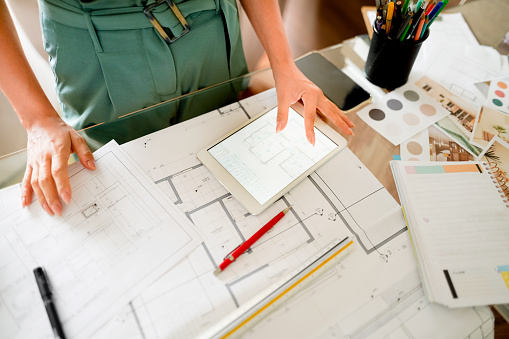 Close-up of a female architect working at her desk using digital tablet and reading blueprints at office