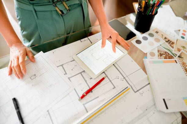 architect working on digital tablet and blueprints at her desk - blueprint office plan paper imagens e fotografias de stock