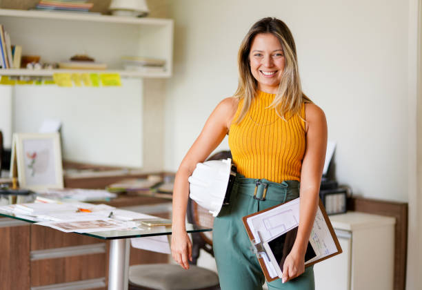 그녀의 사무실에서 하드 햇과 클립 보드와 함께 서 미소 여성 엔지니어 - 토목기사 뉴스 사진 이미지